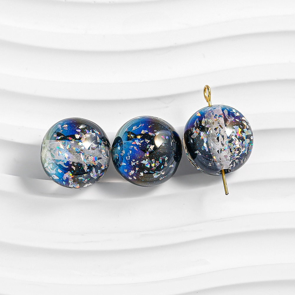 Three blue-black galaxy glitter resin beads on white; right bead has gold loop and pin
