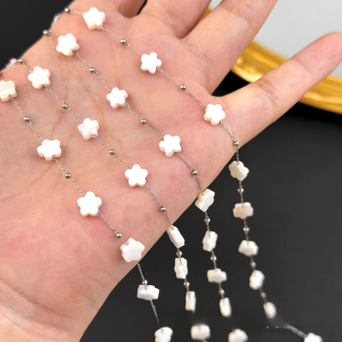 Hand displaying silver station chain with white flower-shaped beads.