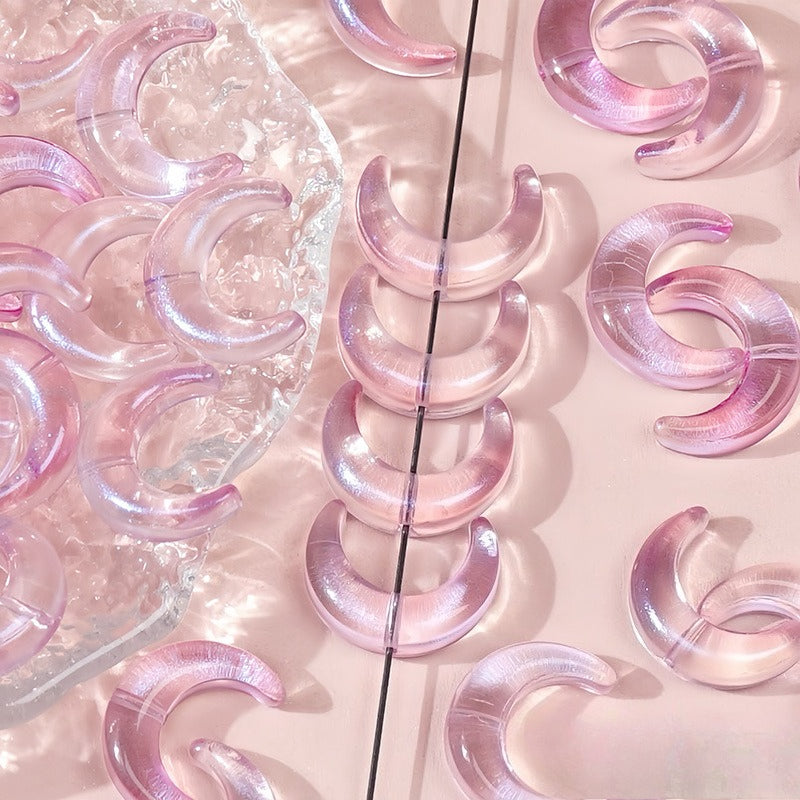 Pink iridescent glazed glass crescent moon beads, some in a clear tray and one strung on a black string