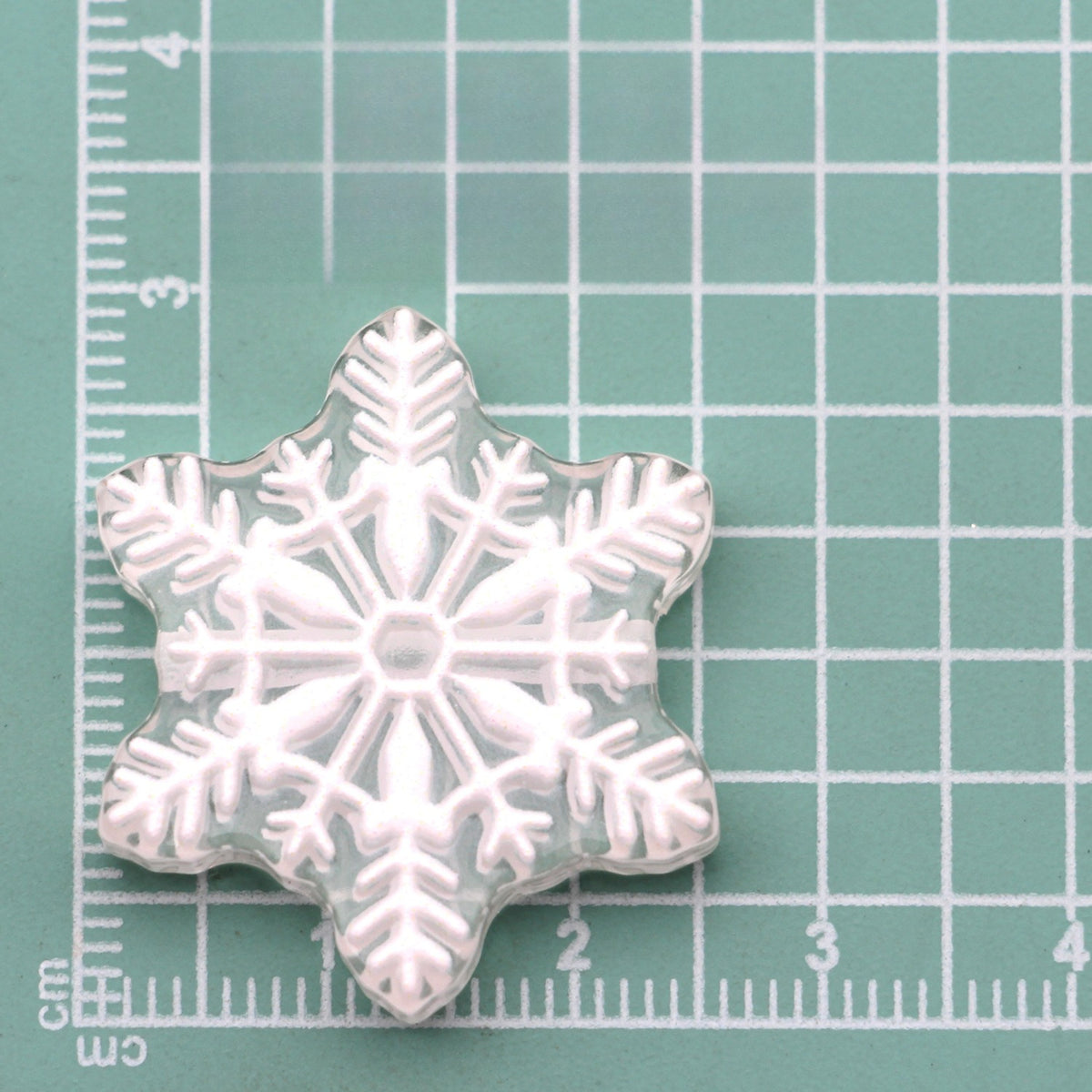 Clear snowflake acrylic charm with white embossed snowflake design on green cutting mat