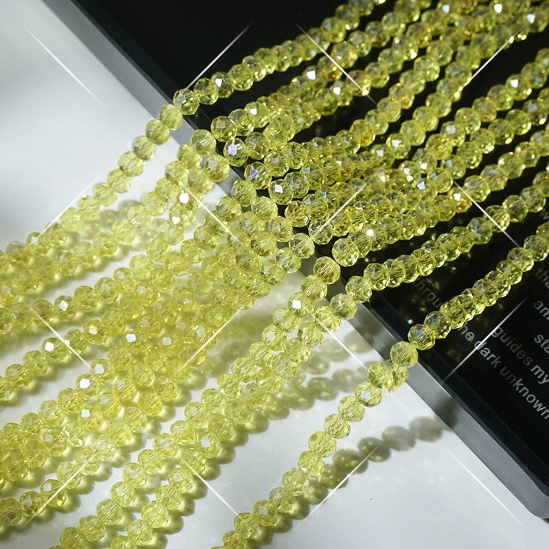 Multiple strands of faceted pale yellow-green crystal glass wheel beads arranged diagonally on white surface