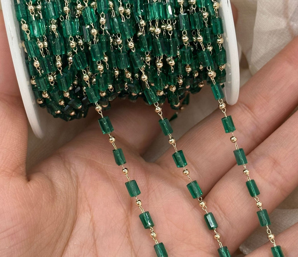 A close-up of a hand holding a spool of green faceted glass beads with small gold spacer beads, showing the strand draped over the palm.