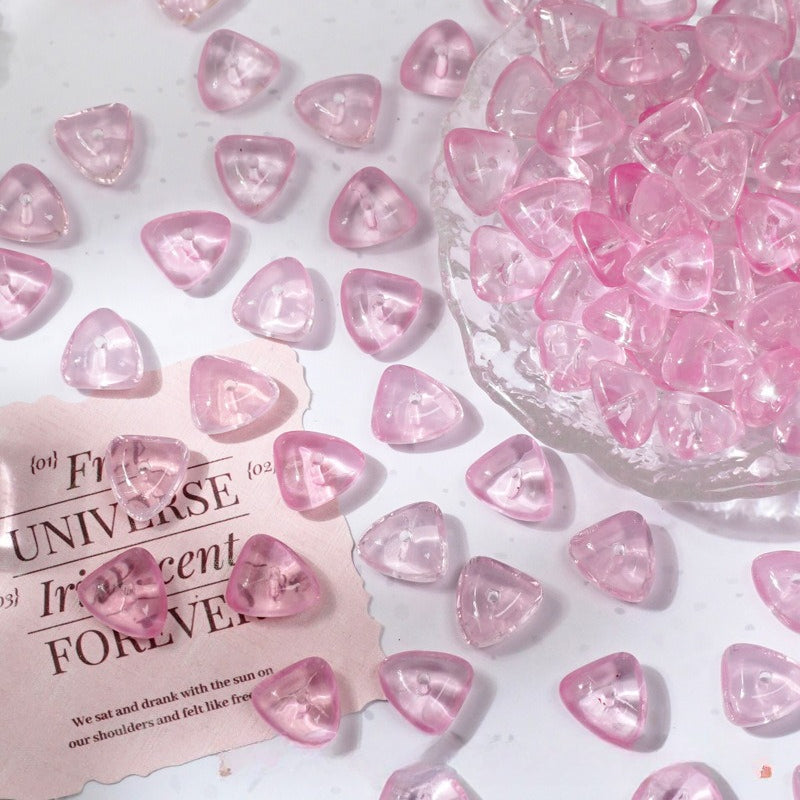 Pink translucent triangular glass beads scattered on a white surface with a glass bowl