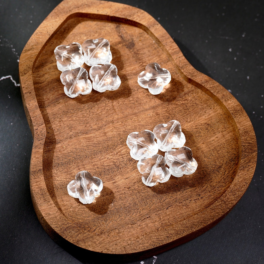 Five clear heart-shaped glass beads on a rustic wooden tray against a dark background