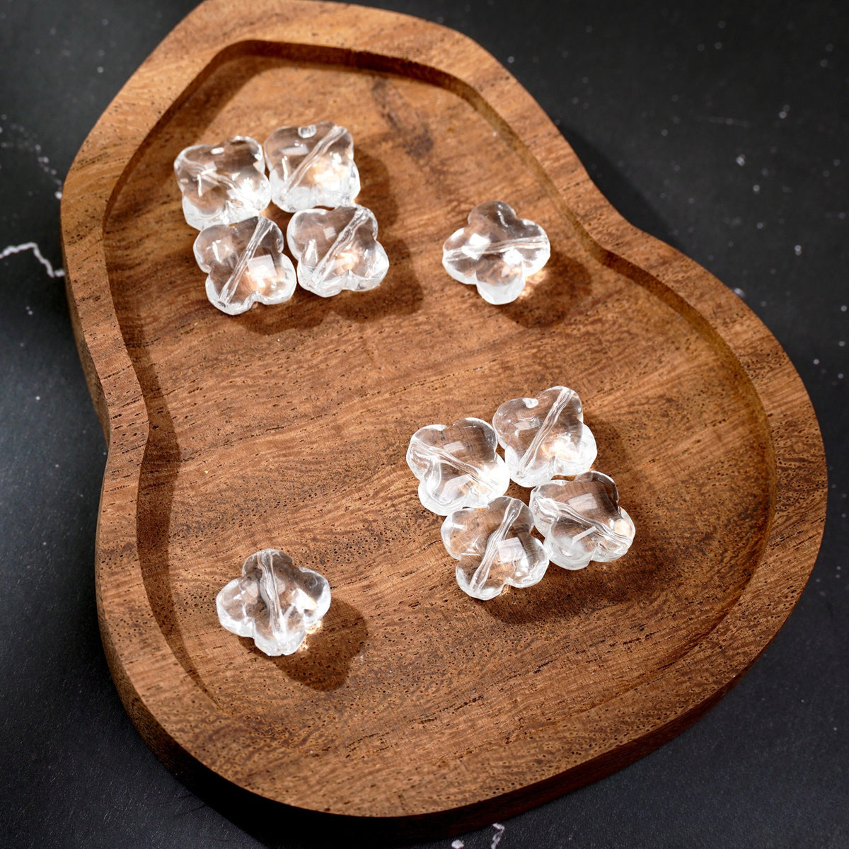 Five clear heart-shaped glass beads on a rustic wooden tray against a dark background