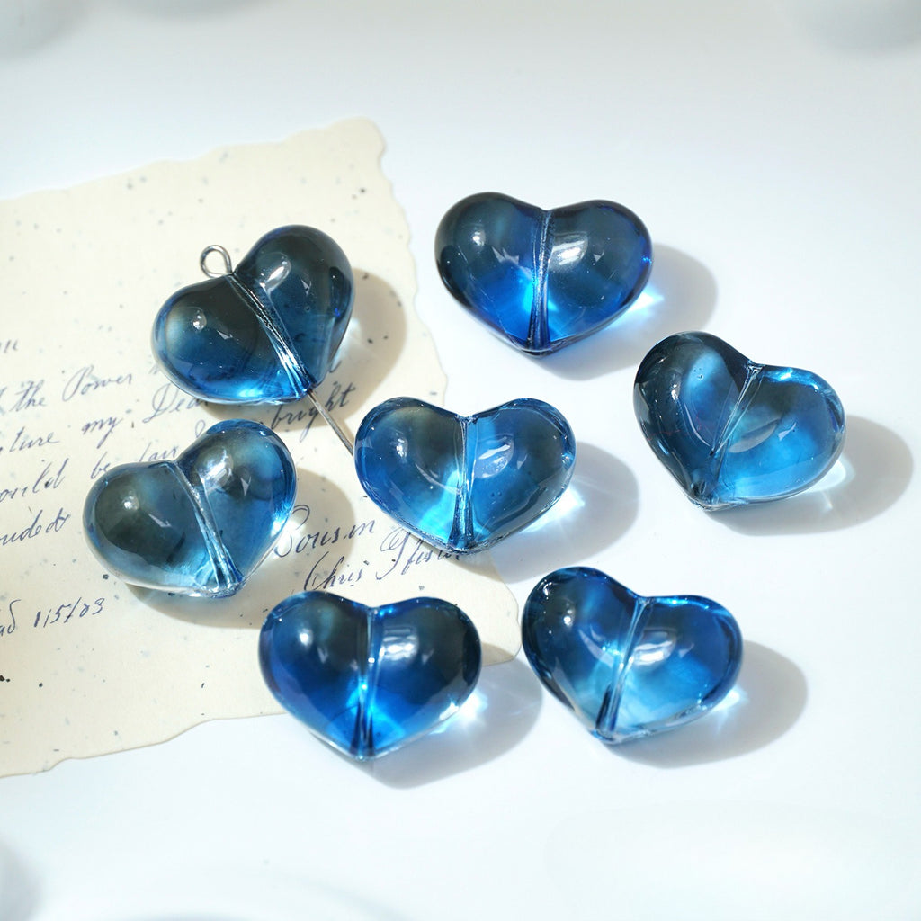 Five translucent blue heart-shaped glass beads on a white surface
