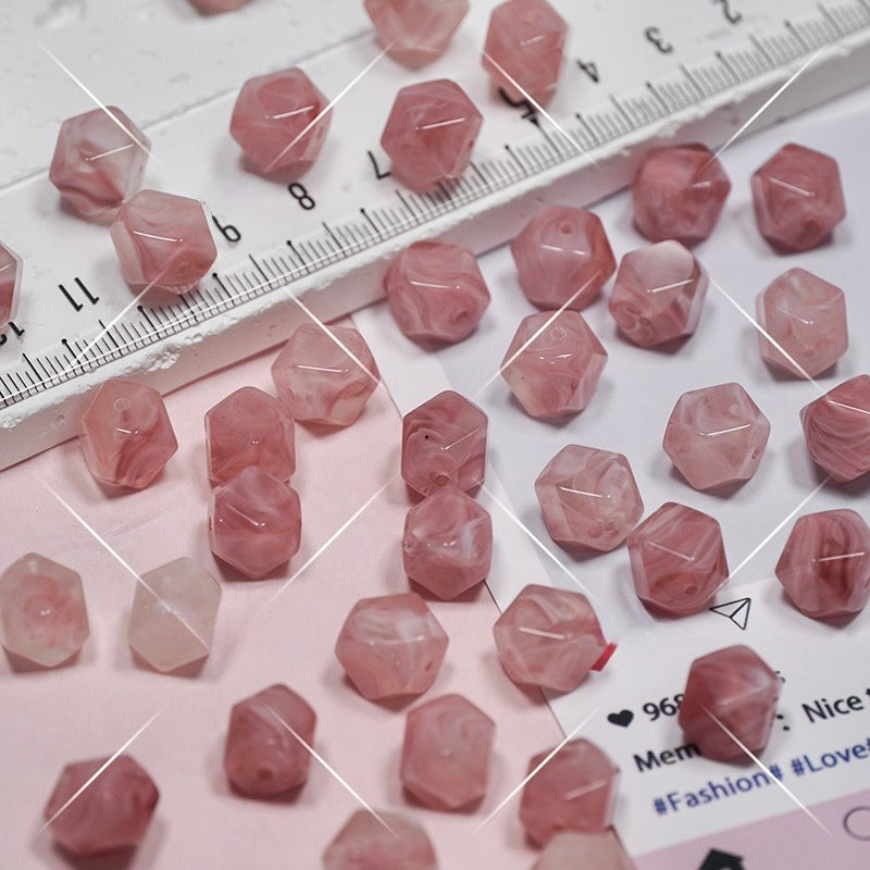 Faceted pink beads scattered on a white surface with a ruler for scale