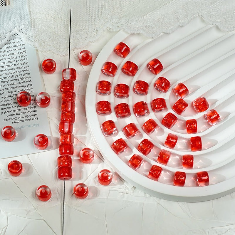 Red translucent glitter barrel beads on a white spiral tray with loose beads and a beaded strand nearby