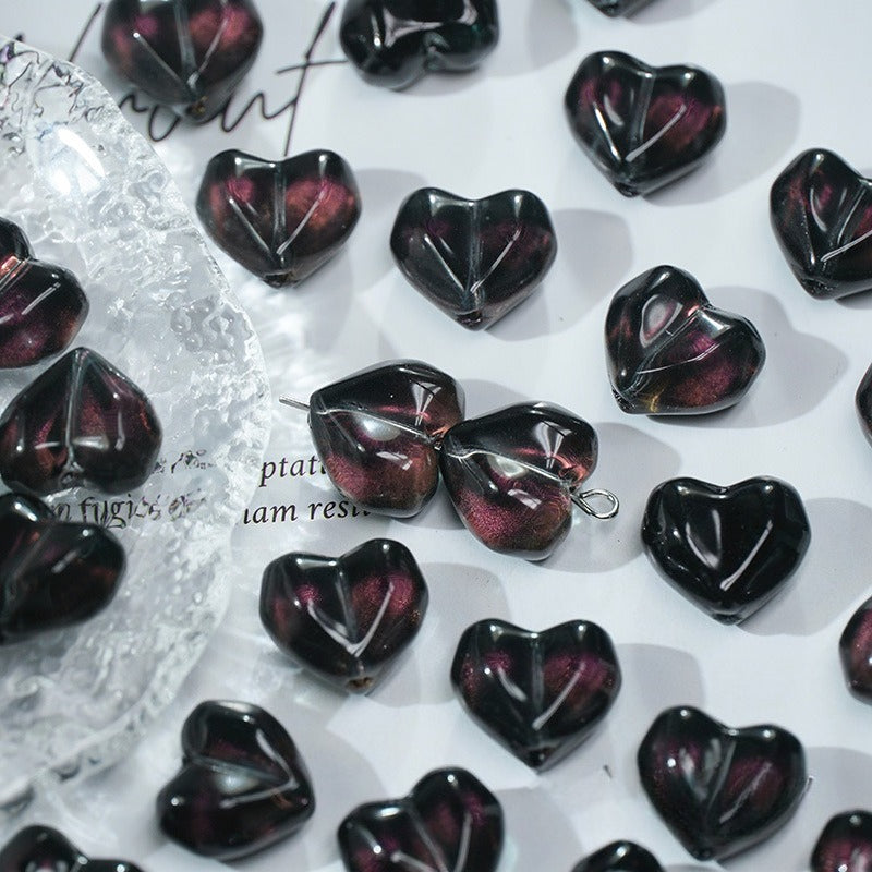 Black heart-shaped glass beads with deep purple shimmer on a white background with a clear textured dish