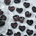 Black heart-shaped glass beads with deep purple shimmer on a white background with a clear textured dish