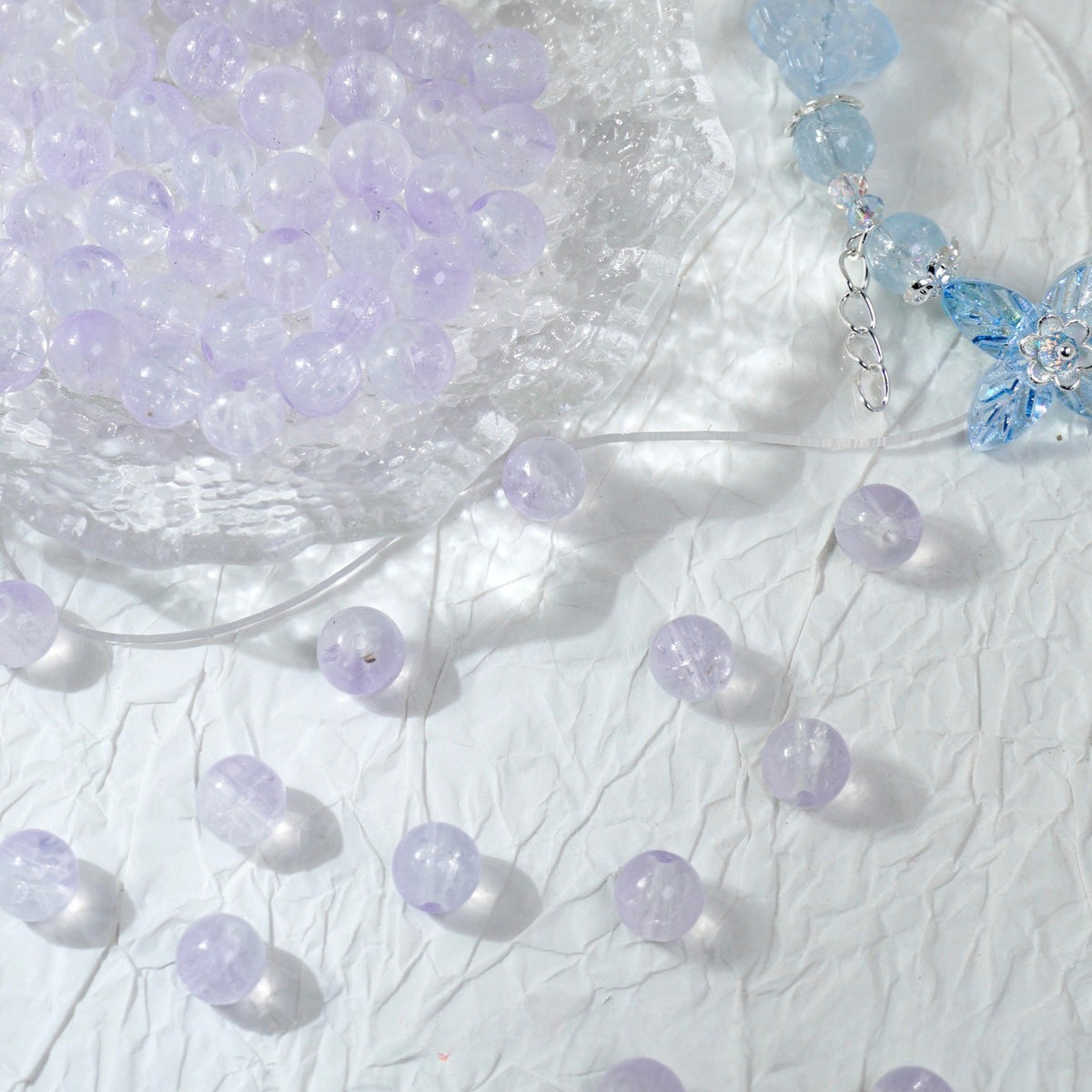 Pale purple translucent glass beads in a bowl with a blue beaded charm accessory