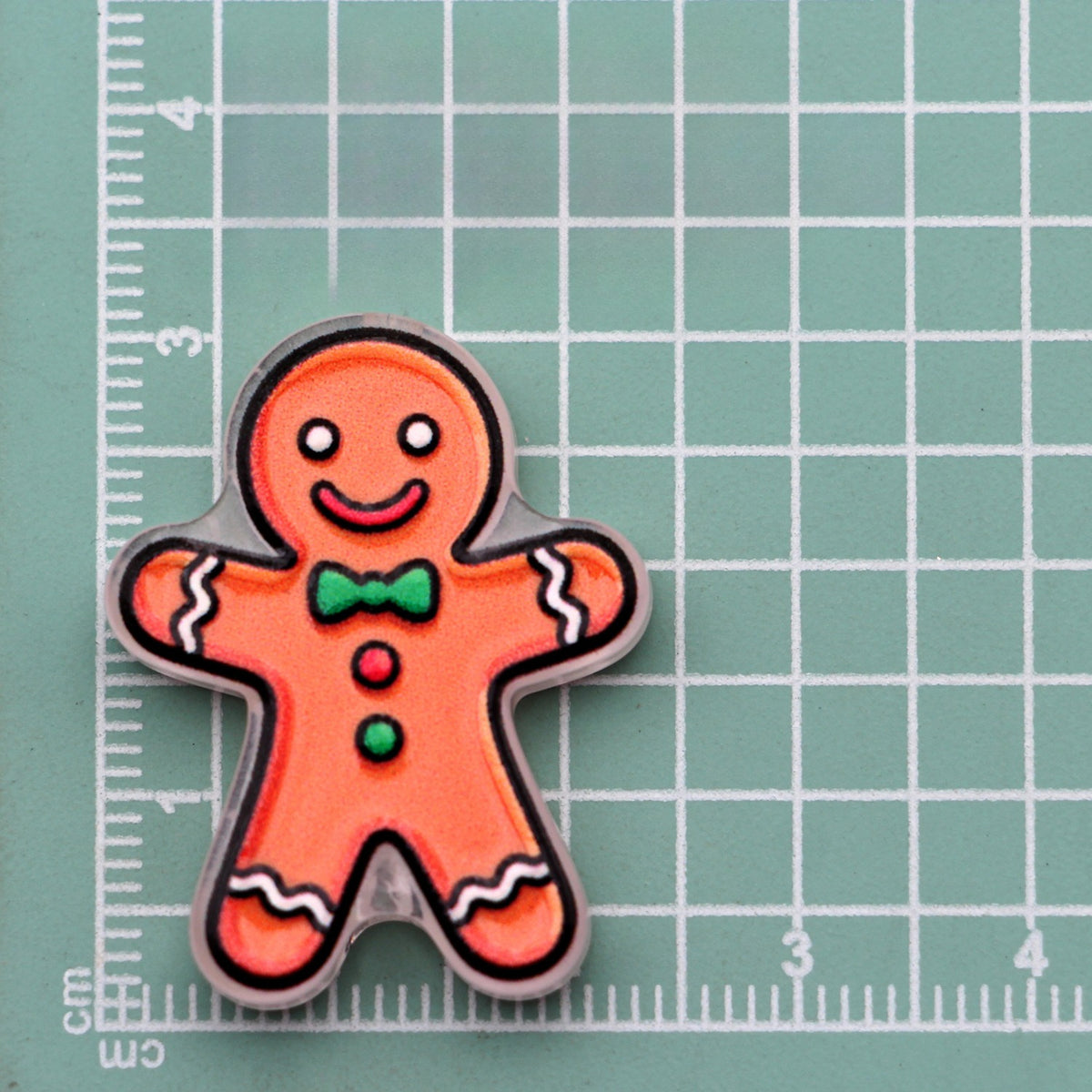 Gingerbread man acrylic charm with green bow tie on green cutting mat