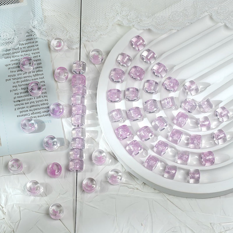 Light purple glitter barrel beads on a white spiral tray with a beaded strand and loose beads scattered