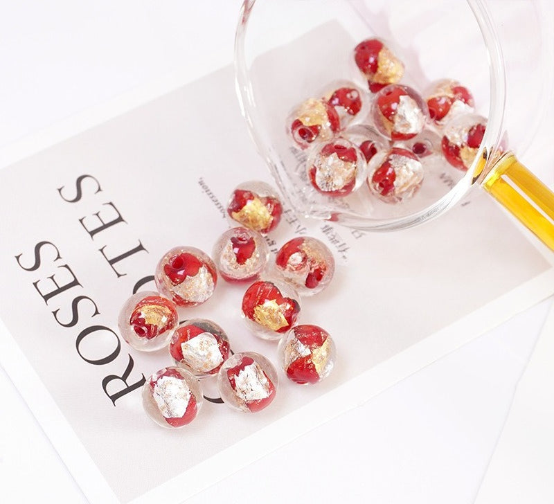 Red and gold-leaf glass beads spilling from a glass scoop onto a printed card