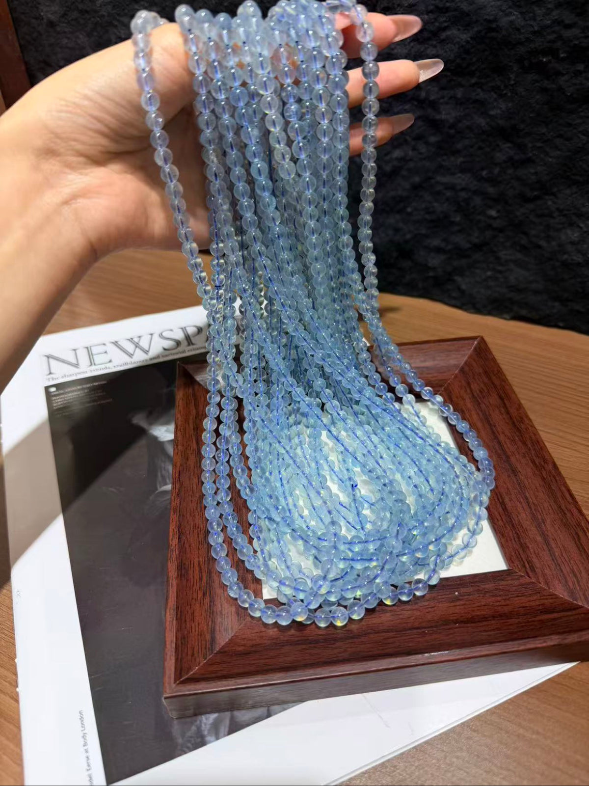 Hand holding long strands of pale blue aquamarine beads draped over a small wooden frame