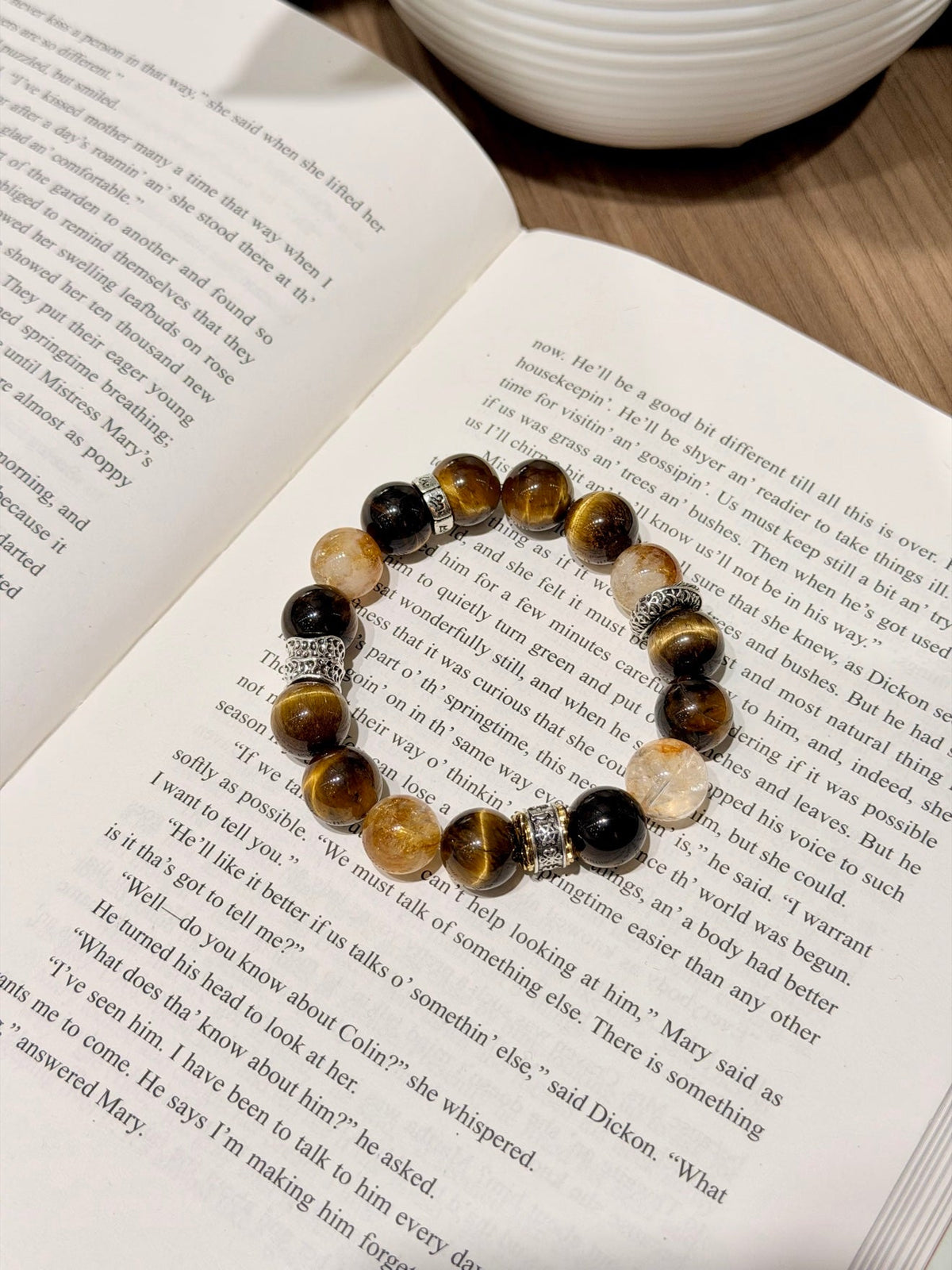 Brown, black and gold-toned beaded bracelet with tiger's eye and quartz beads resting on an open book