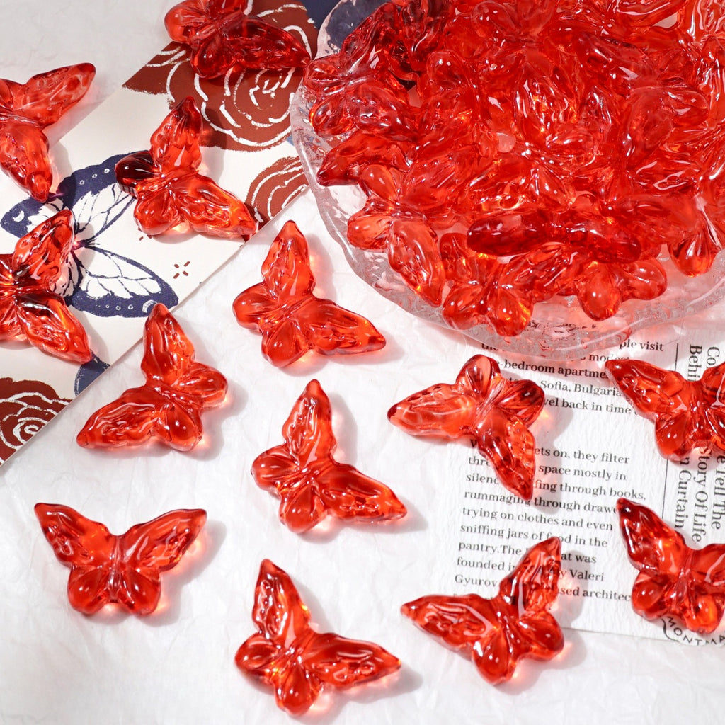 Red translucent butterfly-shaped beads scattered on white surface with glass bowl