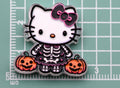 Hello Kitty skeleton acrylic charm with black and pink bow, skeleton outfit, and two pumpkins on green cutting mat