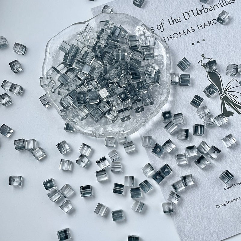 Clear transparent crystal glass cube beads scattered on white, glass dish filled