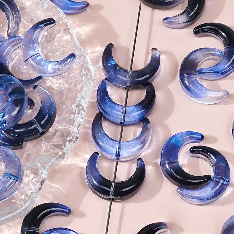 Blue gradient glazed glass crescent moon beads, some strung on a wire and others resting on a clear dish