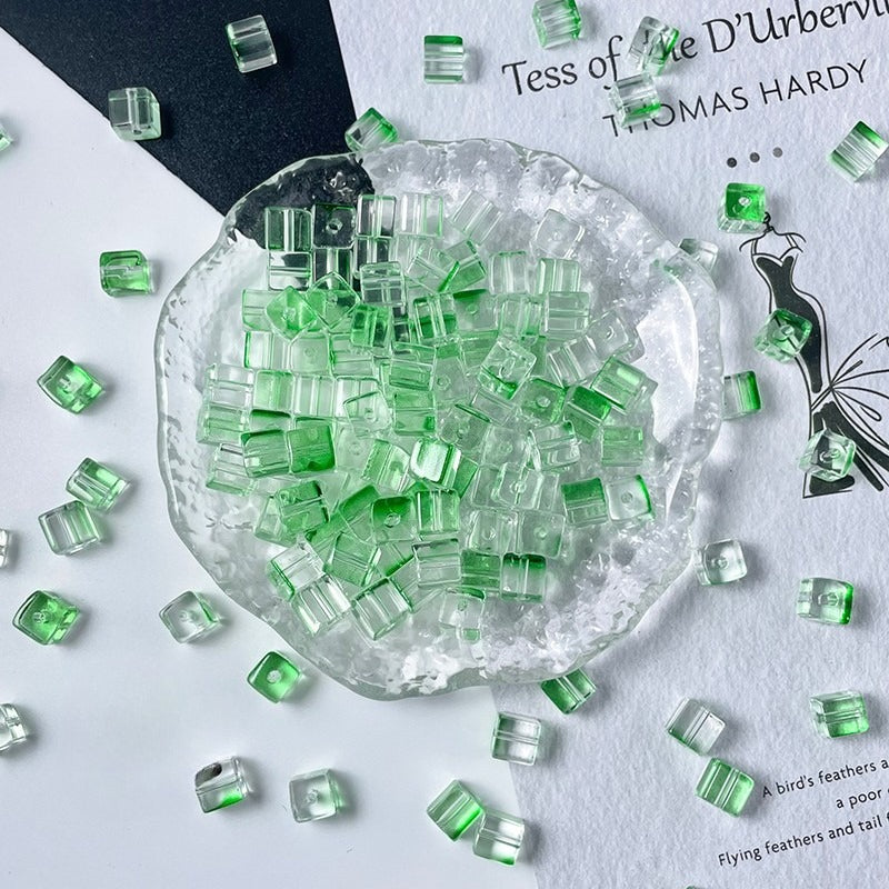 Clear glass cube beads with vibrant green centers in glass dish