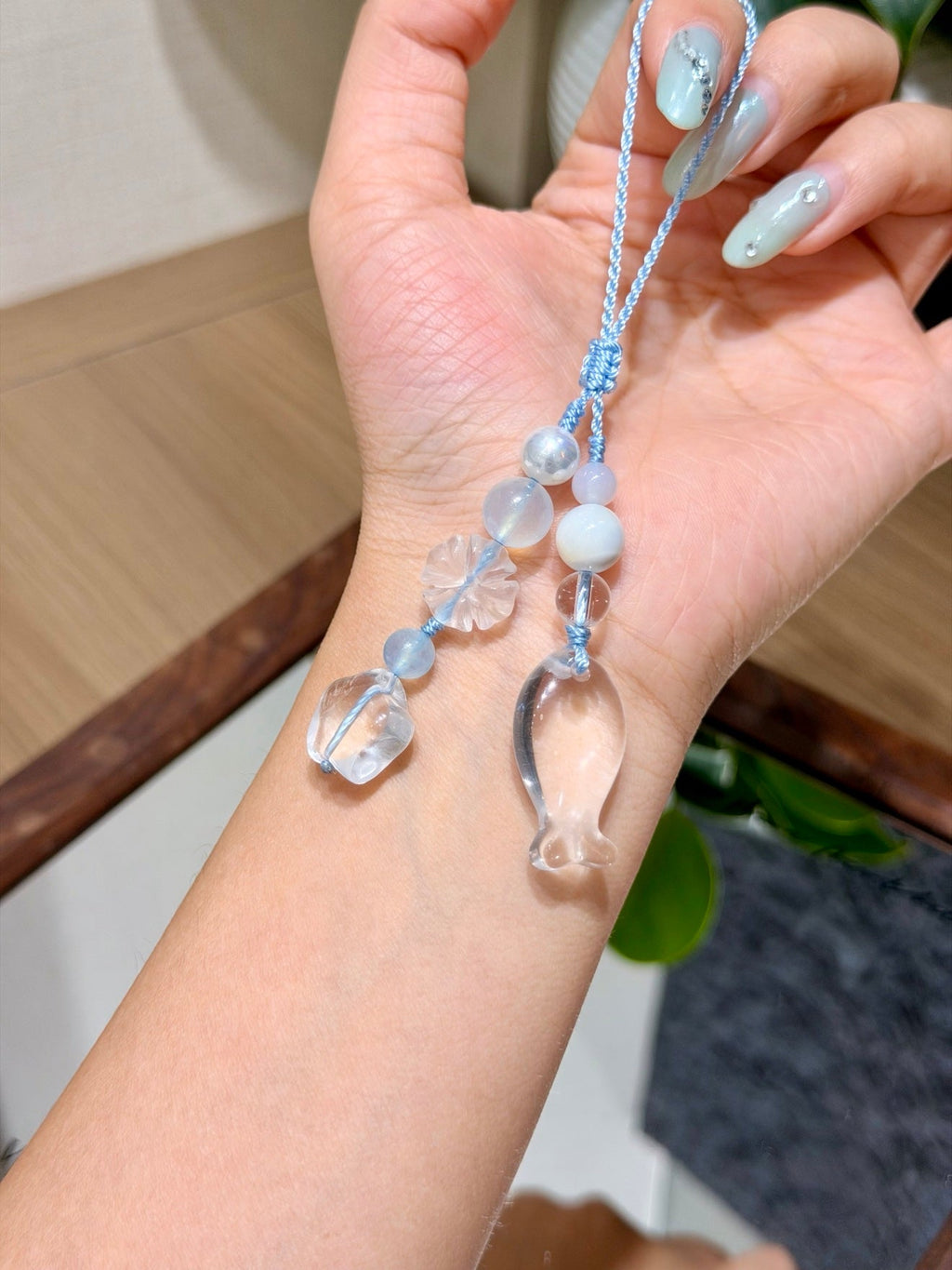 Hand holding light blue cord phone charm with clear glass beads and fish pendant.