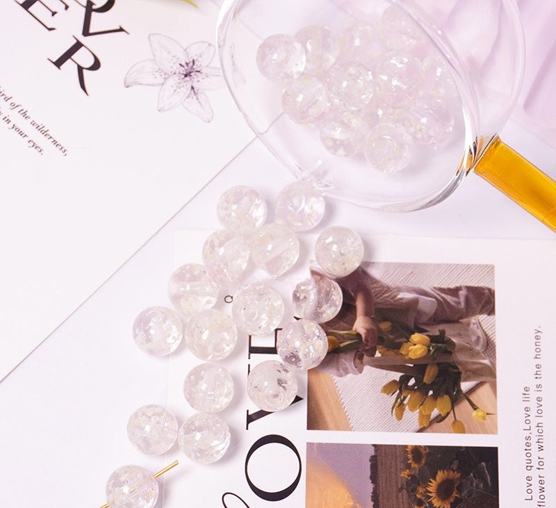 Clear white two-tone glow-in-the-dark glass beads spilling from a glass cup onto a printed card