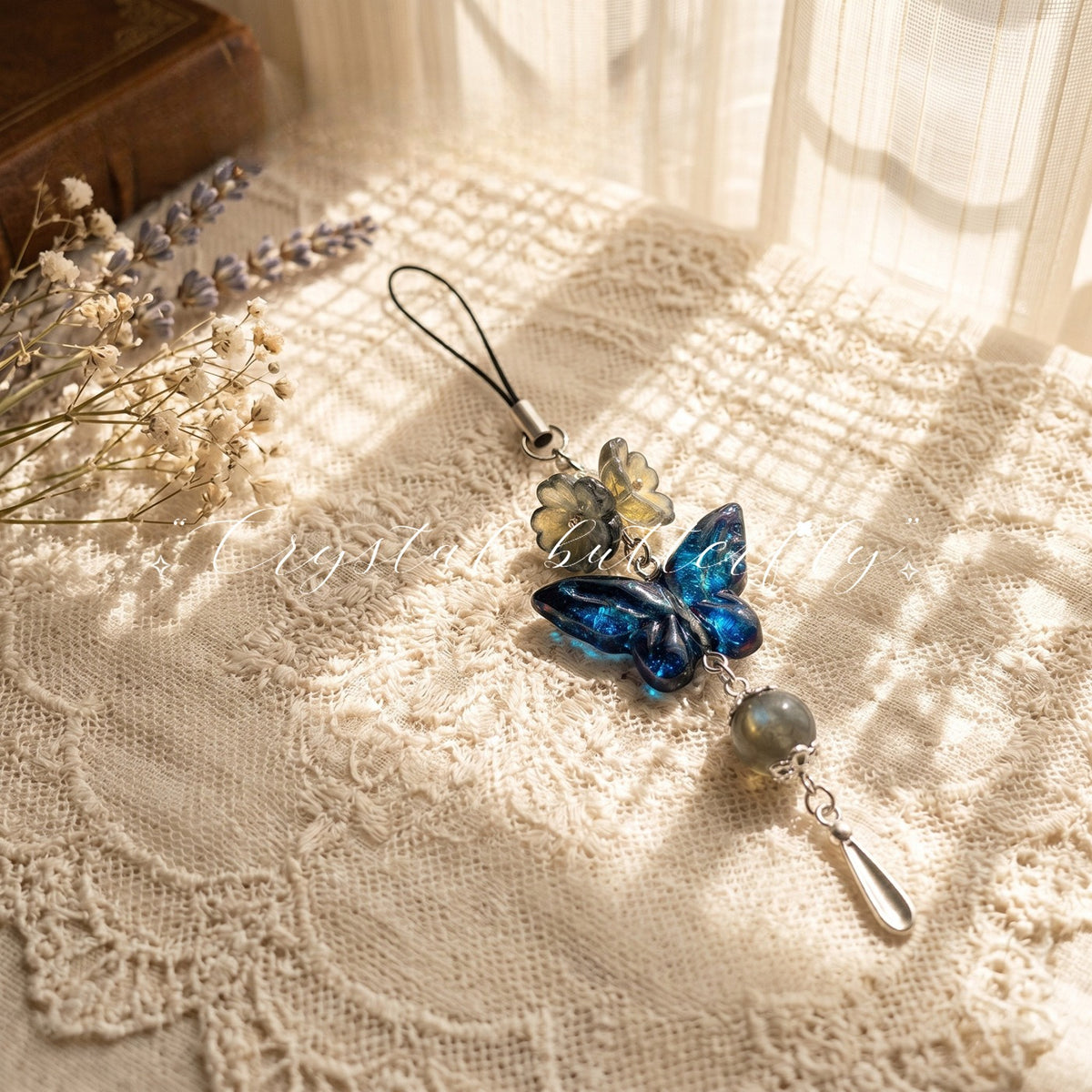Butterfly charm with blue and gold translucent wings, gray pearl bead and silver teardrop pendant on cream lace