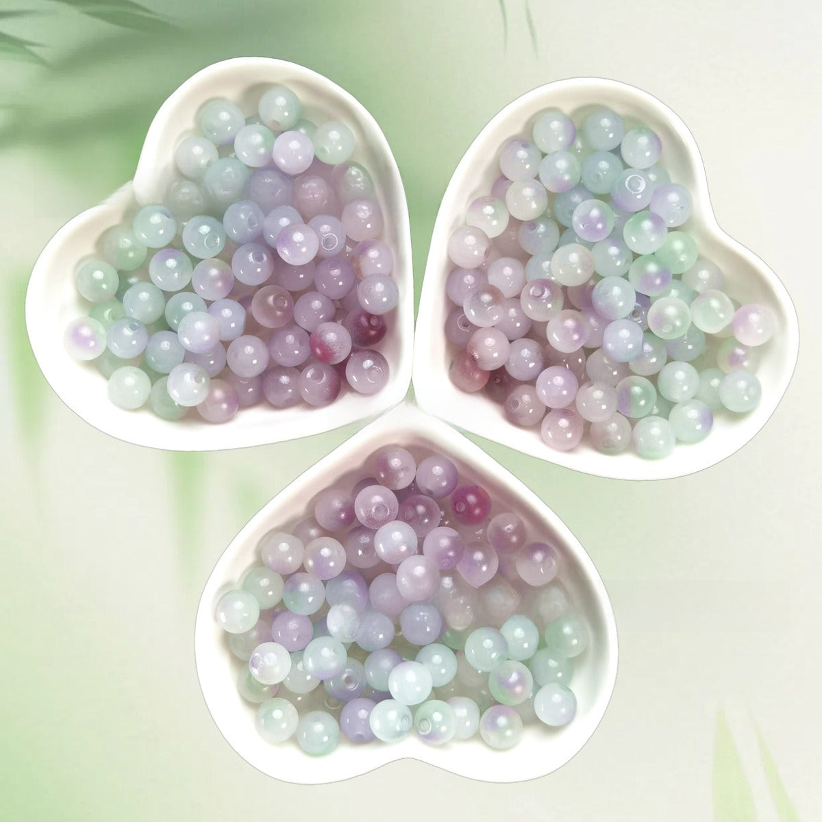 Three heart-shaped bowls of iridescent pastel lavender, mint, and purple beads