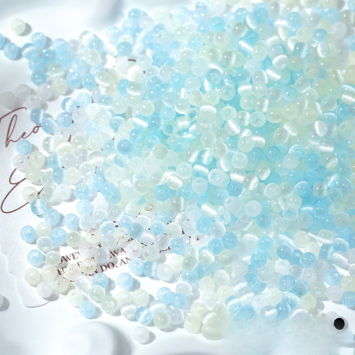 Close-up pile of frosted pale-blue and white cat's-eye glass beads on white surface
