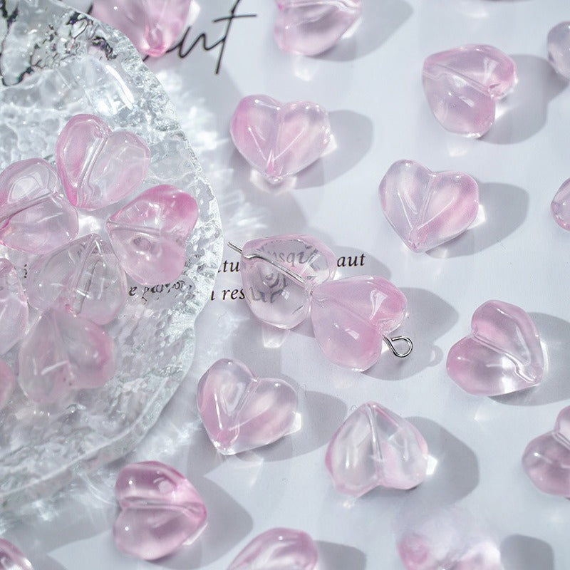 Pink translucent heart-shaped glass beads scattered on a white surface with a clear dish