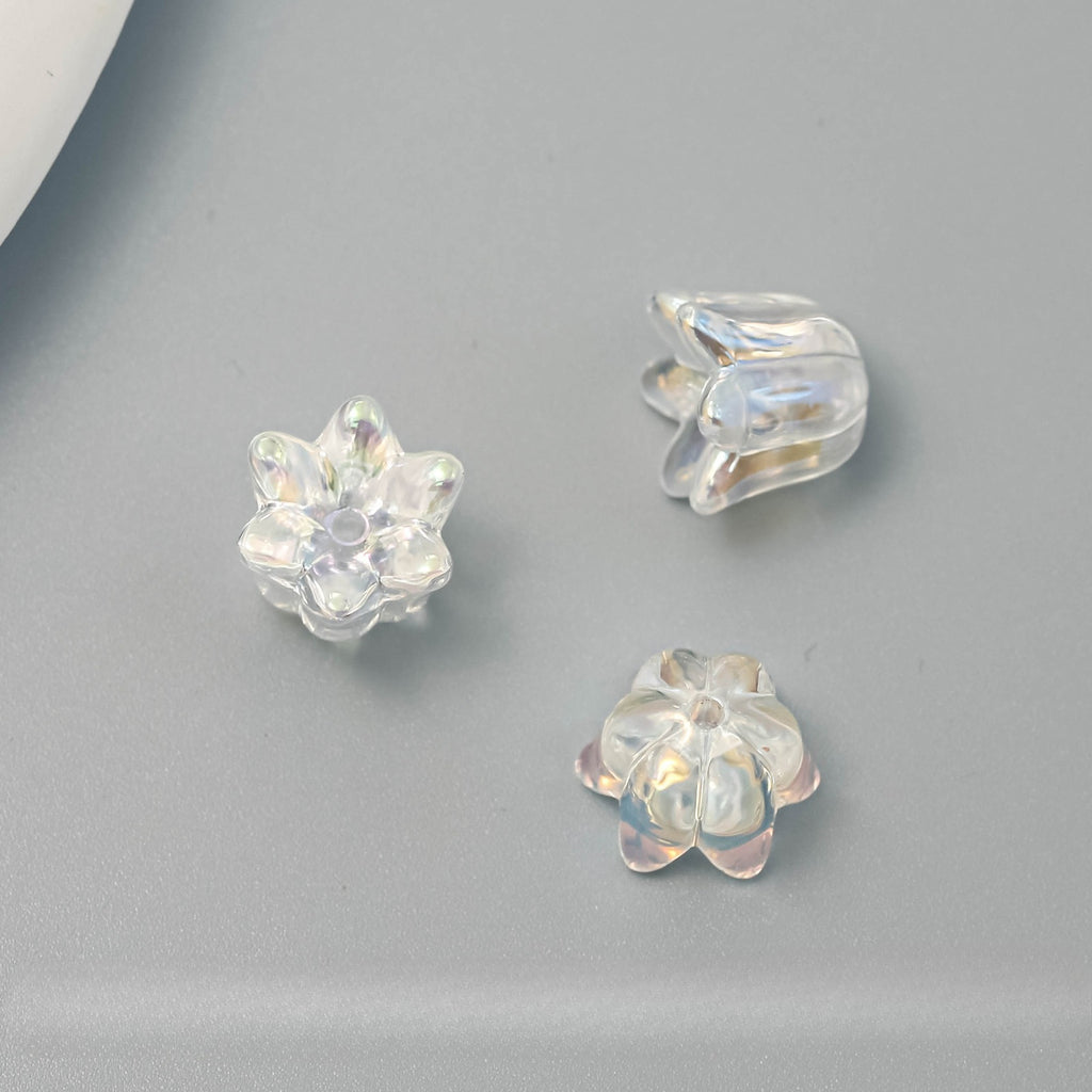 Three clear, iridescent flower-shaped craft beads arranged on a smooth gray surface.