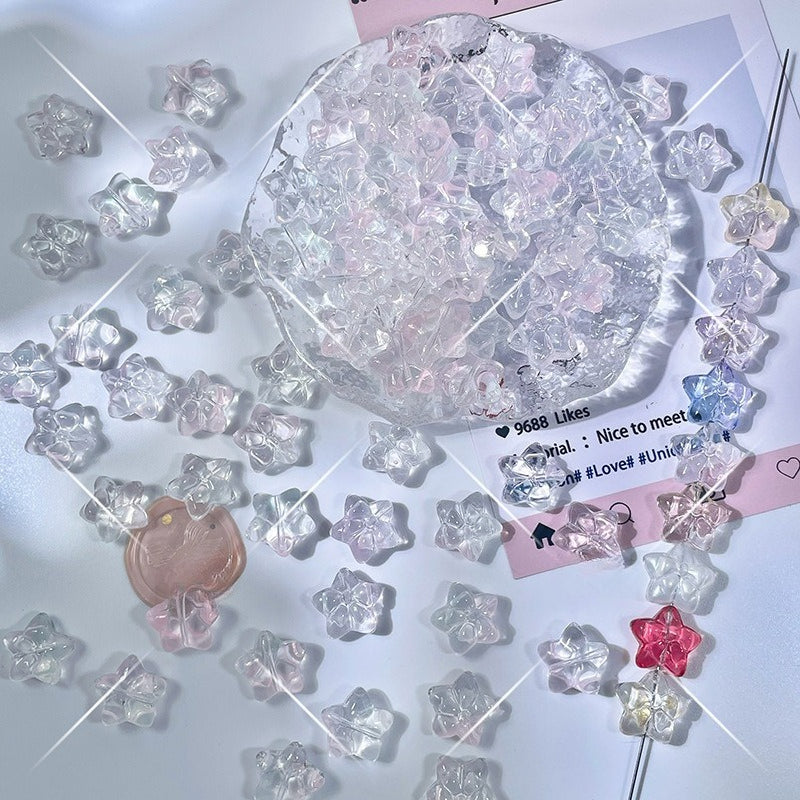 Clear translucent star-shaped glass beads in pink, blue, and red tint on a white surface