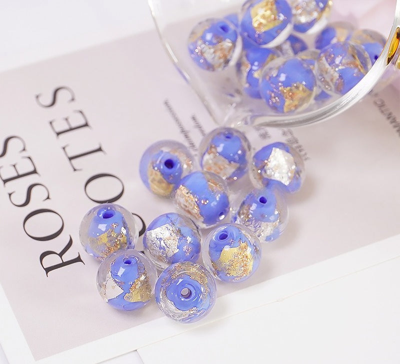 Blue and gold-foil glass beads spilling from a glass container onto a printed card
