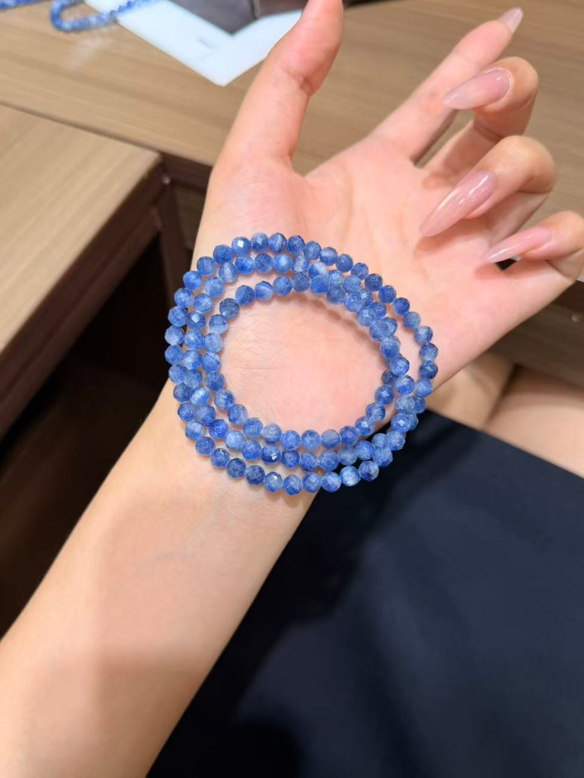 Triple-wrap bracelet of small blue faceted kyanite beads worn on a wrist.