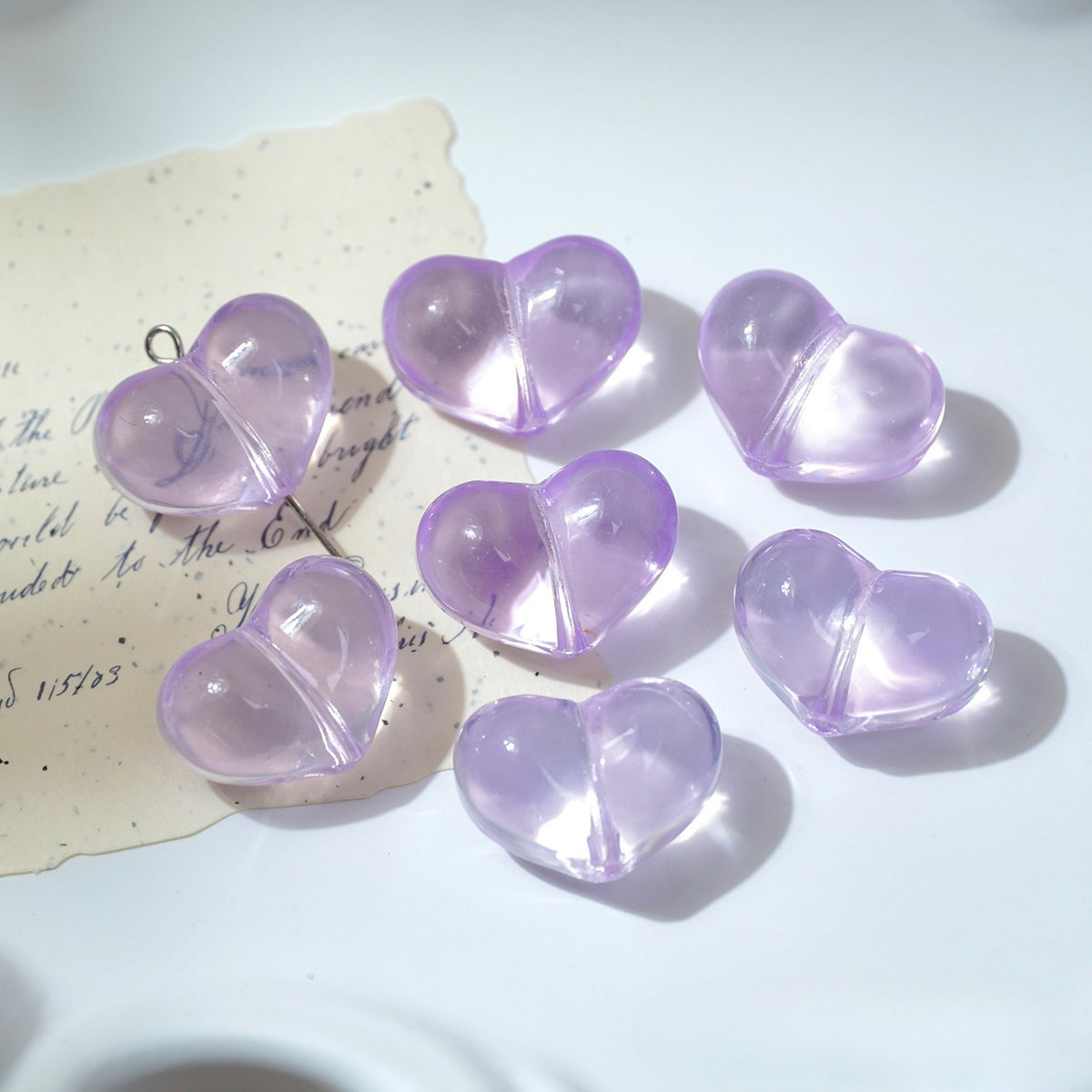Seven translucent lavender heart-shaped glass beads with metal loops on white