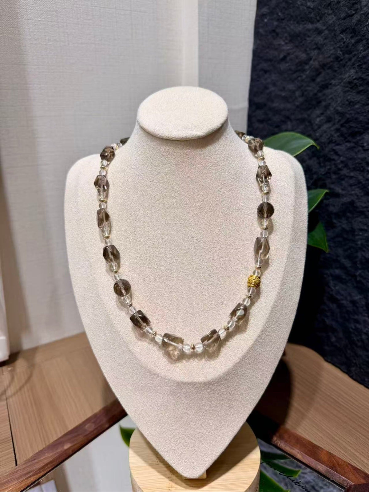 Smoky quartz beaded necklace with faceted brown and clear beads and gold spacers on a display bust