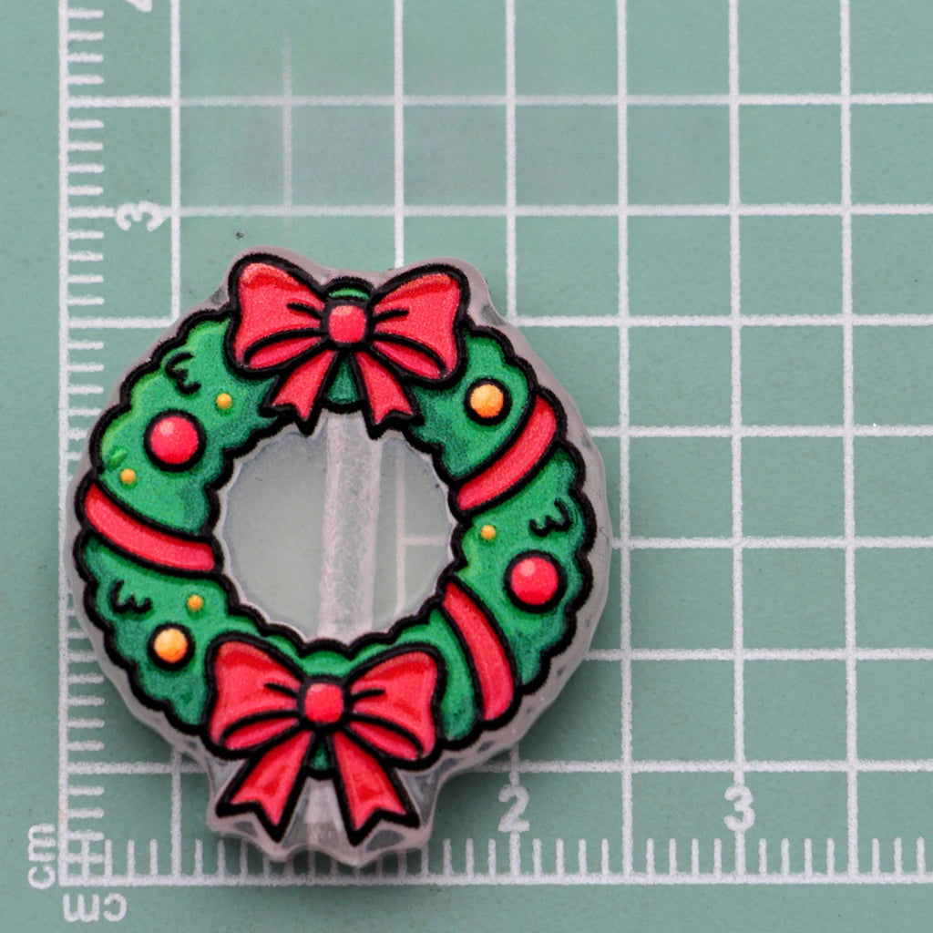 Christmas wreath acrylic charm with red bows, ribbon, and ornaments on green cutting mat