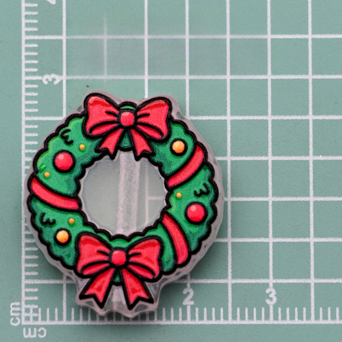 Christmas wreath acrylic charm with red bows, ribbon, and ornaments on green cutting mat
