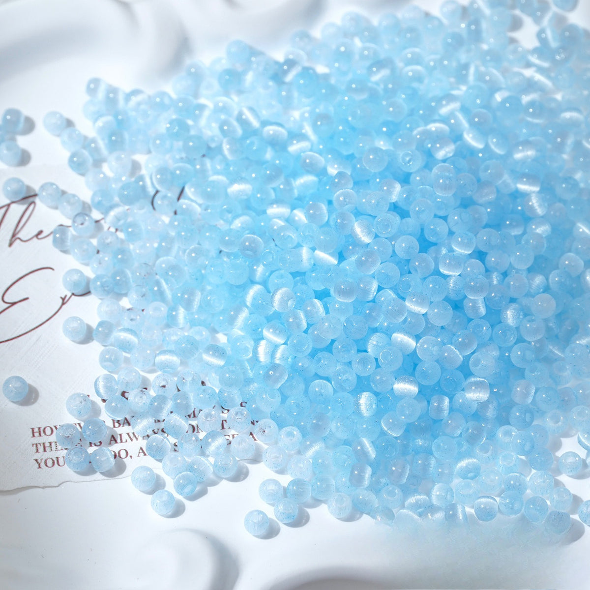 Close-up pile of frosted light-blue cat's-eye glass beads on white surface