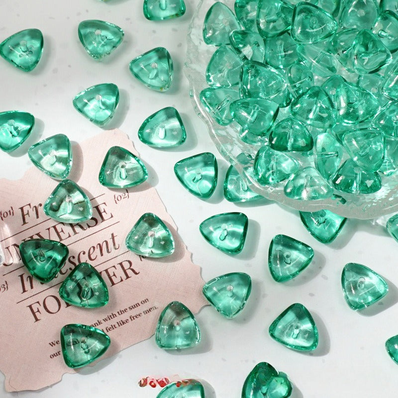 Green translucent triangle-shaped glass beads scattered on a white surface with a glass bowl