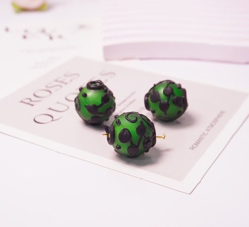 Three green and black patterned bead stud earrings displayed on a printed card on a white surface.