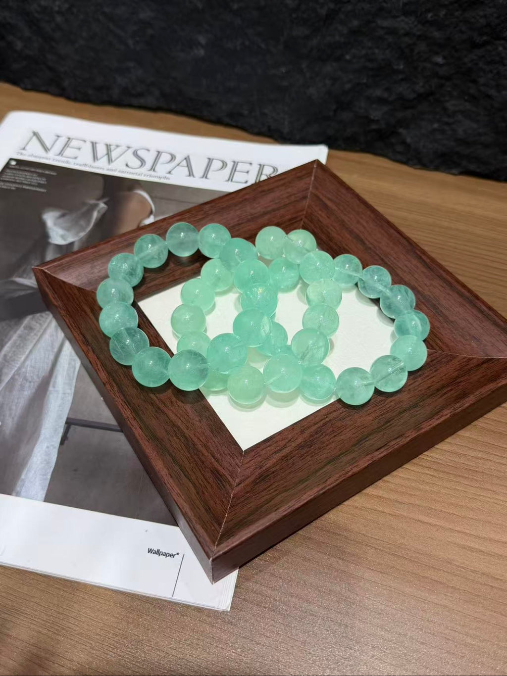 Mint green fluorite bracelet coiled on a square wooden tray