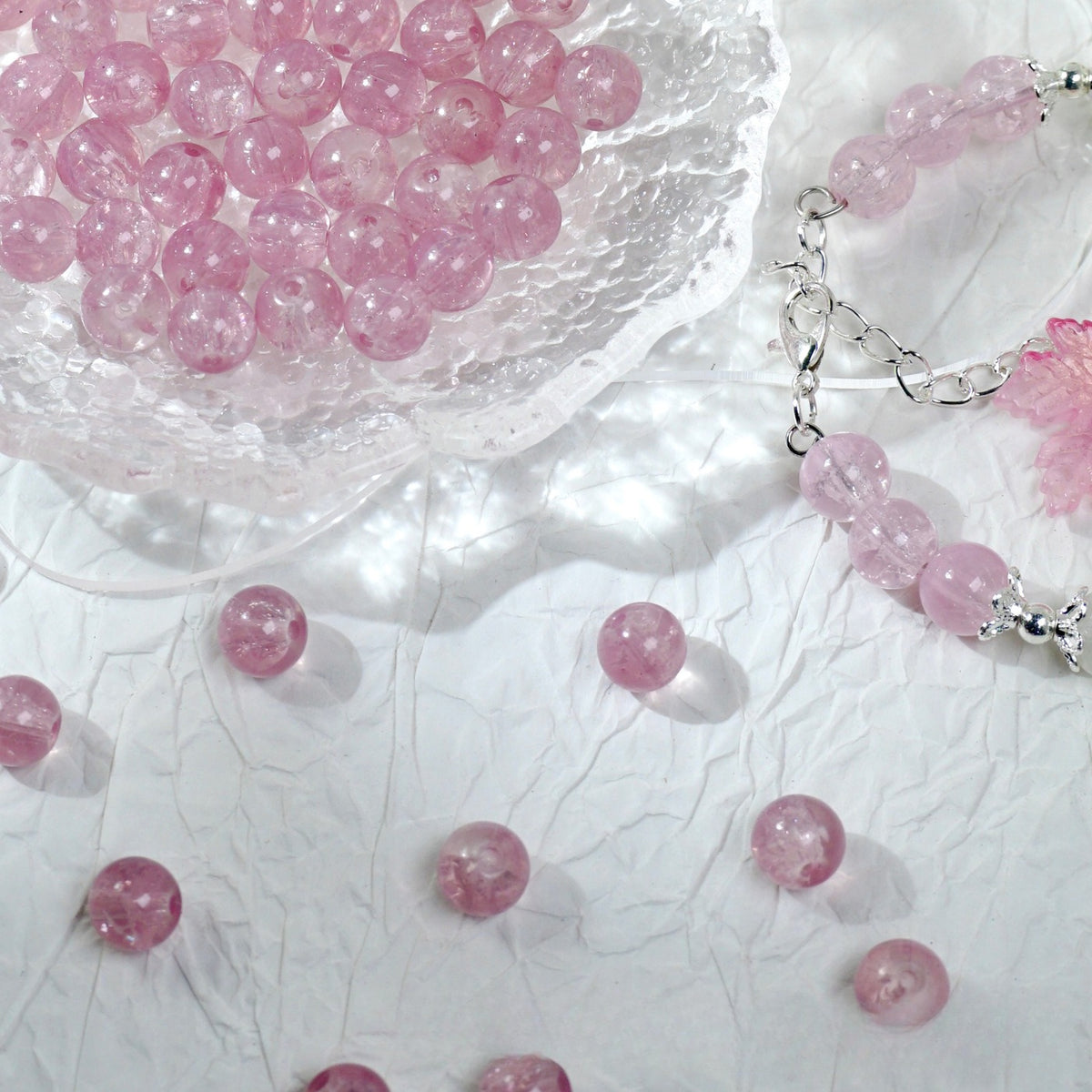 Pink translucent glass round beads in a bowl, scattered with a bracelet