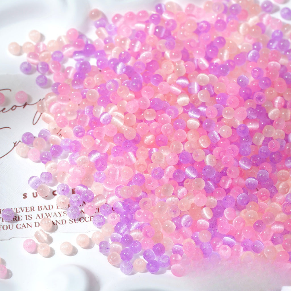 Close-up pile of frosted pastel pink and purple cat's-eye glass beads on white surface
