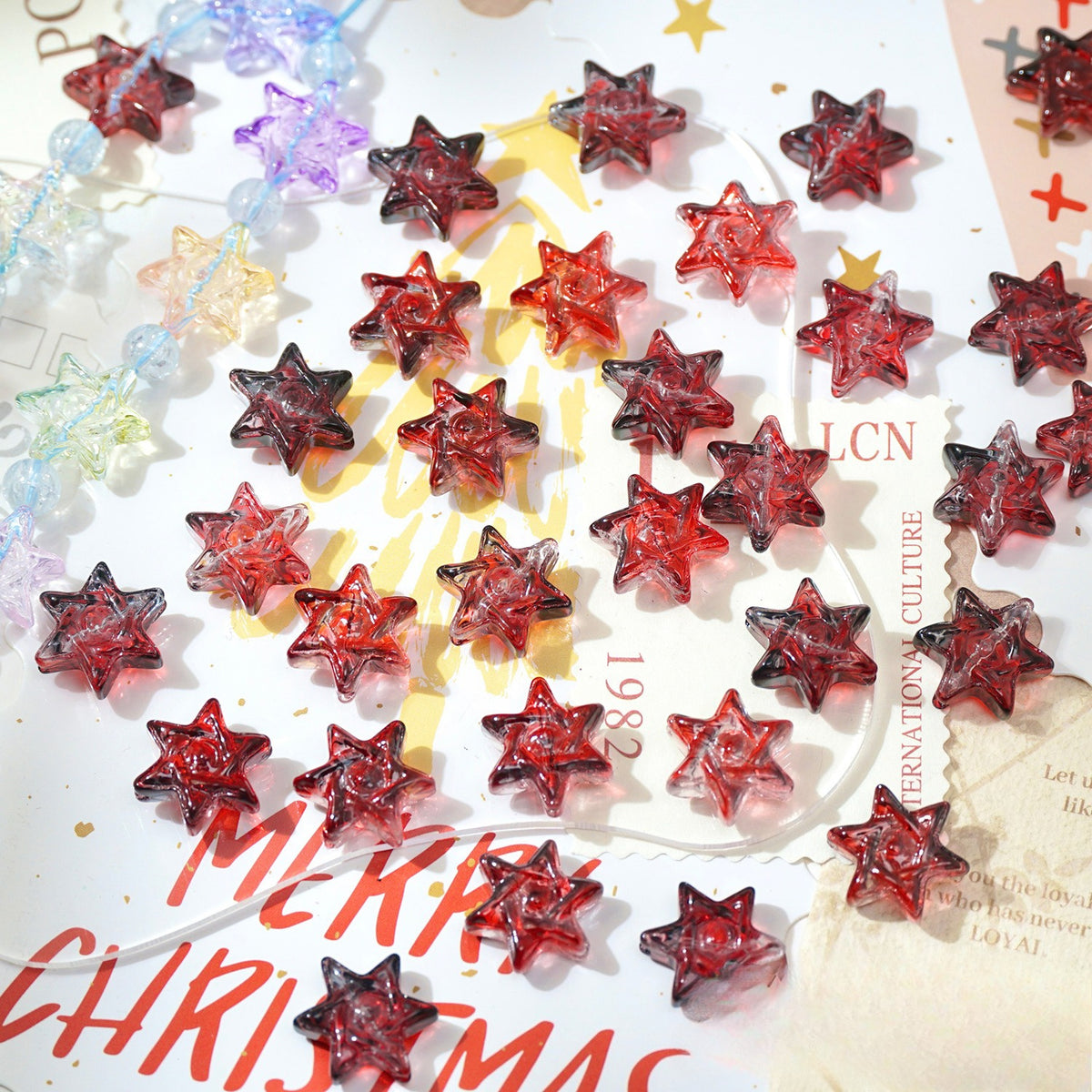 Red translucent star-shaped glass beads scattered on Christmas-themed paper