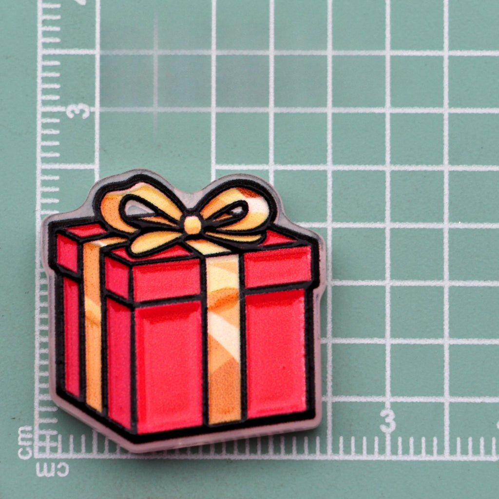 Red gift box acrylic charm with gold ribbon and bow on green cutting mat