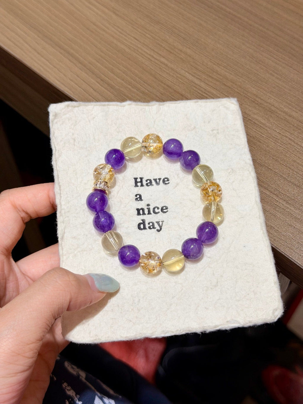 Amethyst and citrine beaded bracelet on a 'Have a nice day' card held in hand