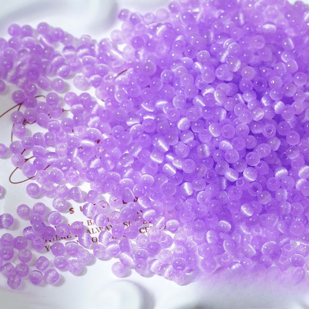 Close-up pile of frosted lavender-purple cat's-eye glass beads on white surface