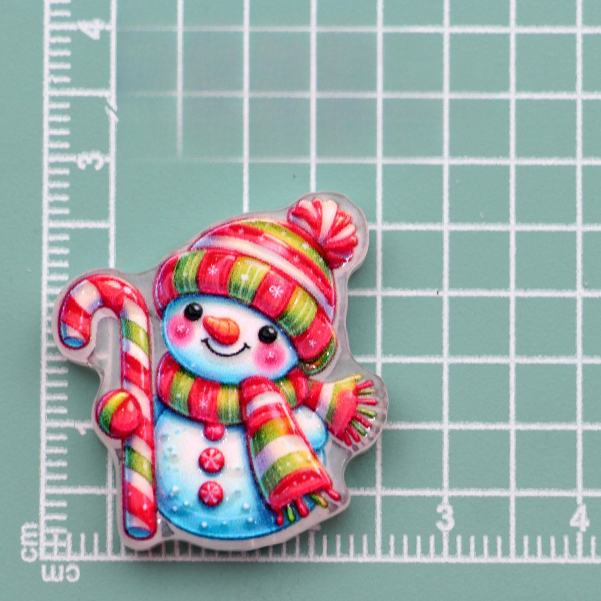Snowman acrylic charm with striped hat, scarf and candy cane on green measuring grid